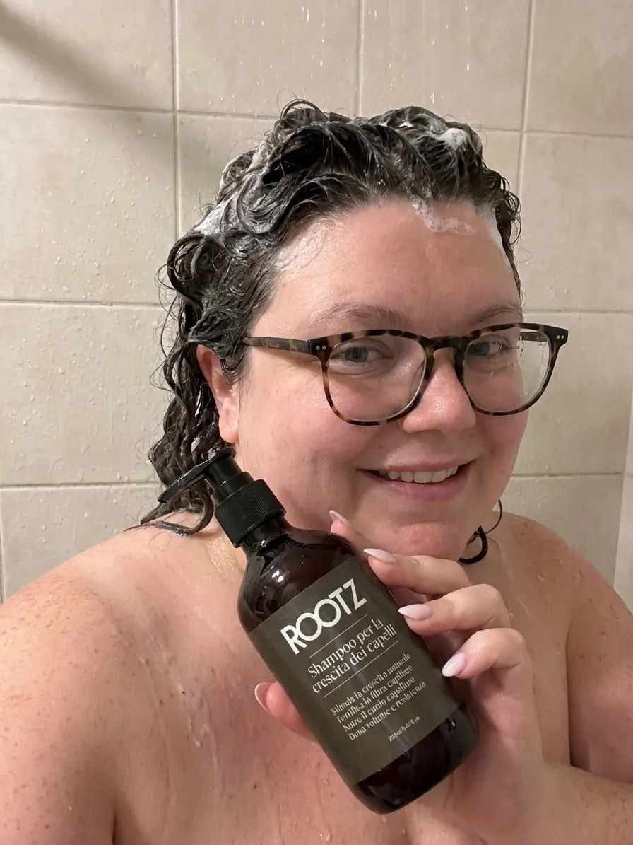 Una cliente si lava i capelli con lo shampoo ROOTZ sotto la doccia, l'etichetta del flacone in vista